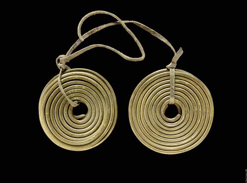 Young and old women’s ear pendant, collected by Kurt Johannes, brass, leather, (a) D: 10,6 cm, (b) D: 10 cm, L: 42 cm (both ear spirals incl. leather cord), 17,5 × 23 × 3,3 cm. III E 4747 a–f, acquired 1896, Ethnologisches Museum, Staatliche Museen z